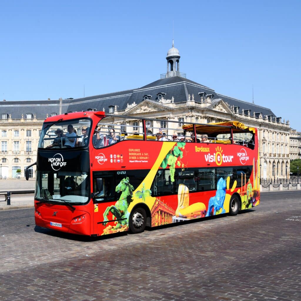 The red double-decker Visiotour hop-on hop-off bus in front of Bordeaux's Place de la Bourse